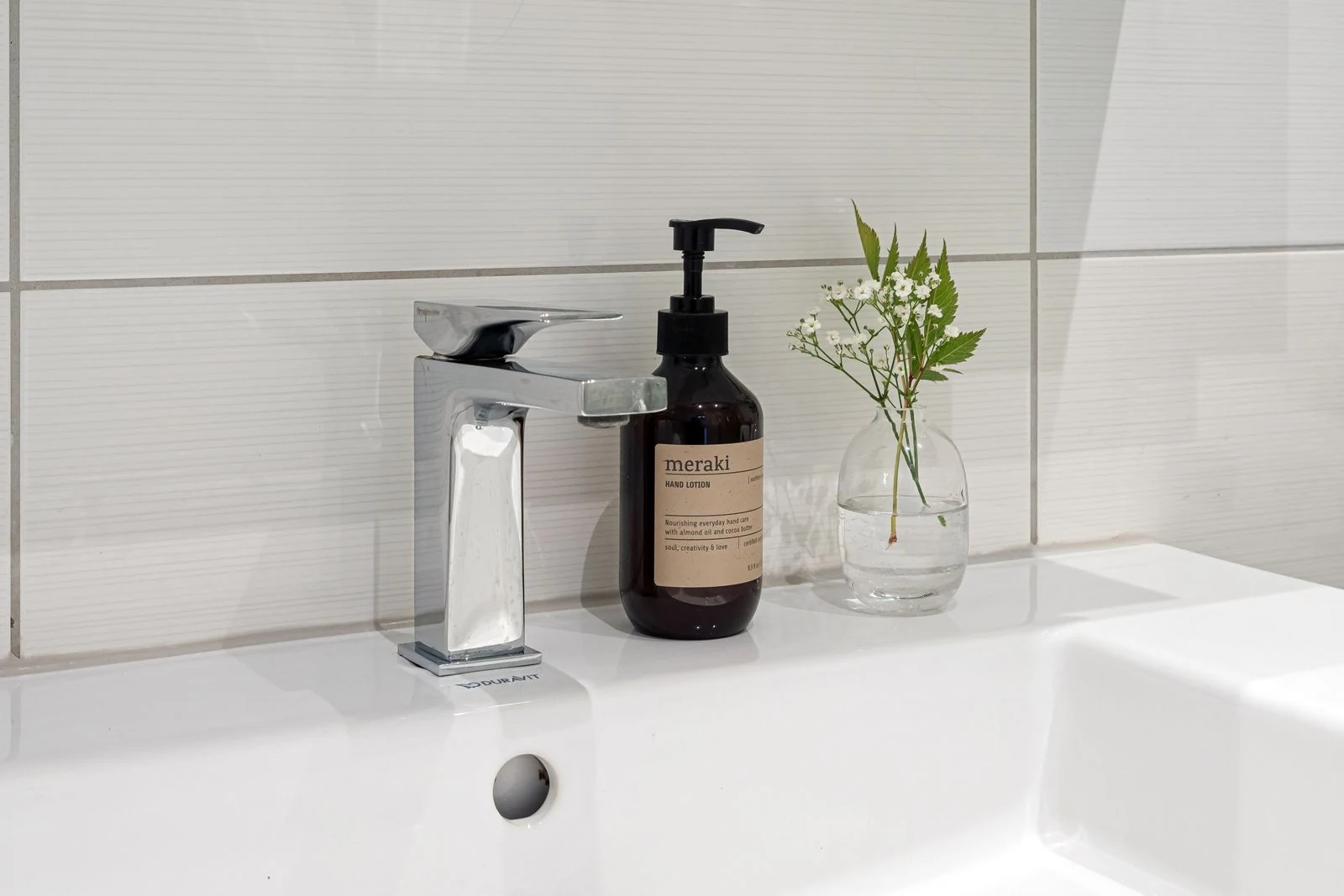 Minimalist bathroom sink setup featuring a soap bottle and vase with white buds, creating a clean look