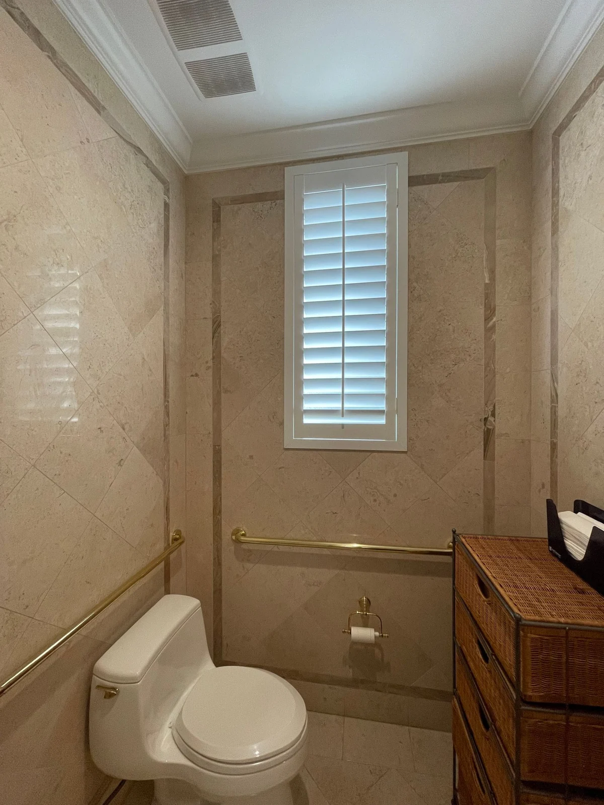 Elegant bathroom interior featuring beige marble tiles, a white toilet, and louvered window. Stylish and compact design