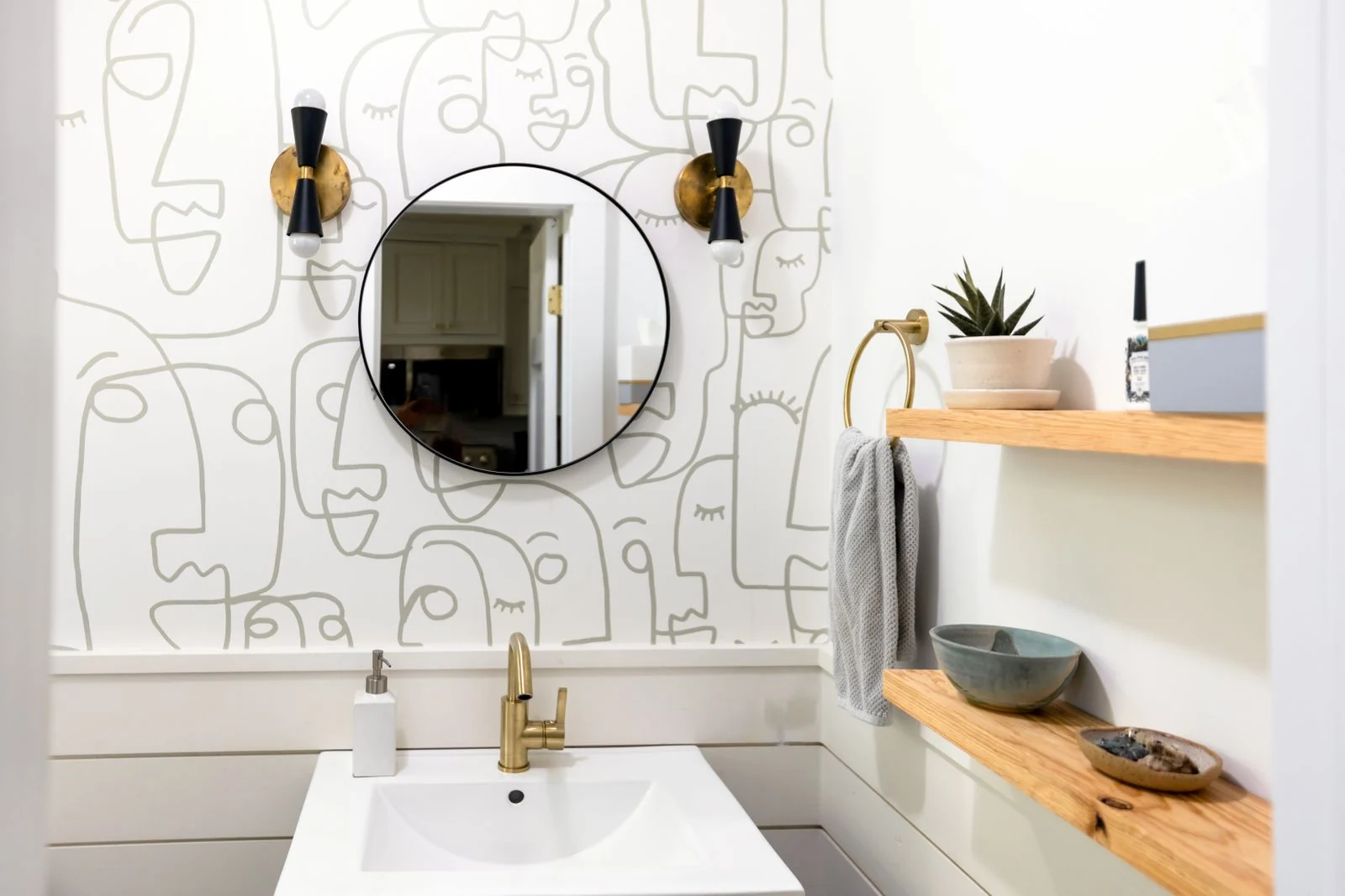 A contemporary bathroom featuring abstract line art wallpaper, round mirror, and minimalist wooden shelves