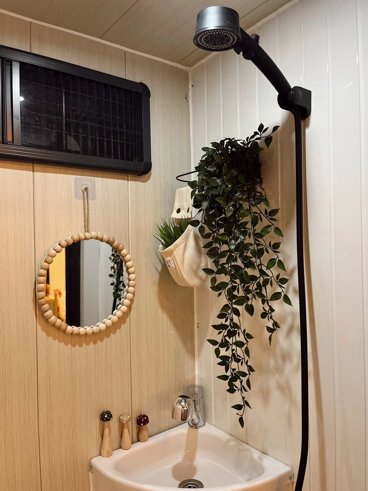 Modern bathroom with a wood-framed mirror, hanging plants, and a sleek showerhead