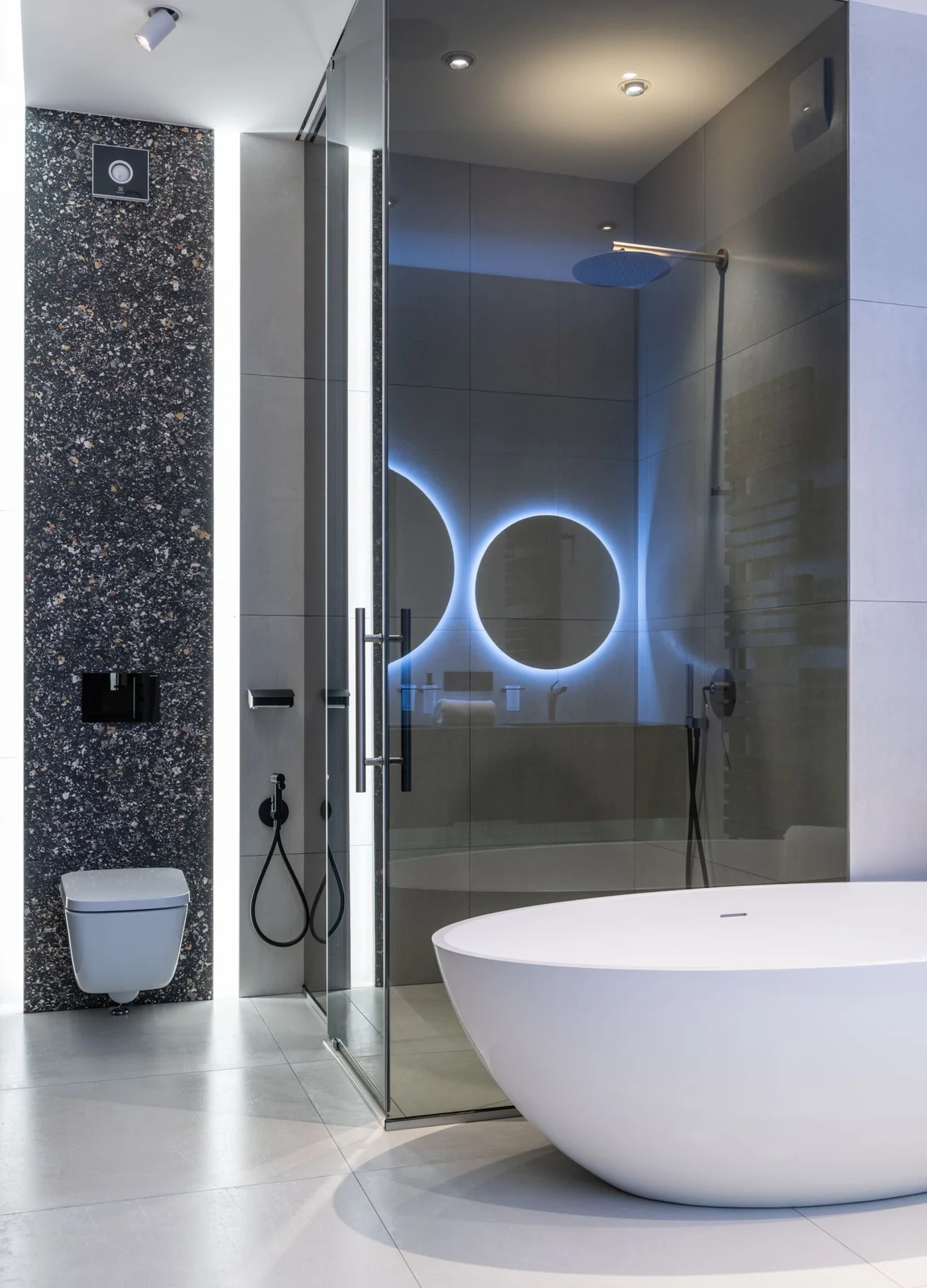 Stylish restroom with oval bathtub and toilet near glass shower with bright illumination