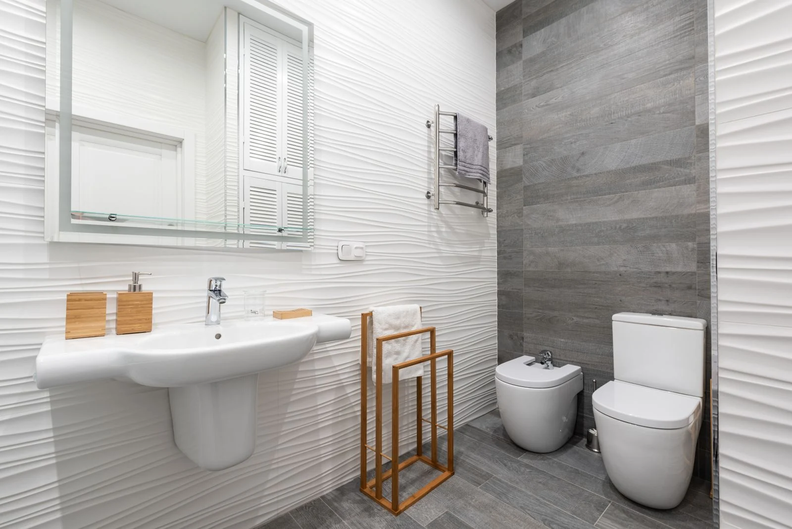 Modern bathroom with washstand under mirror and bidet on ceramic floor with towel on rack at home