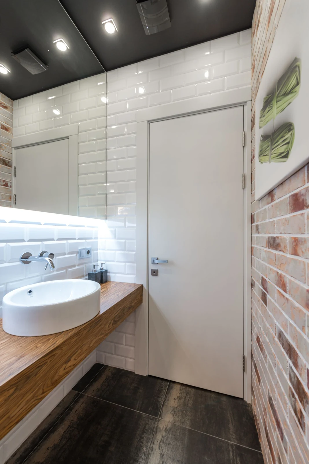 Contemporary bathroom featuring minimalist design with wooden counter, brick wall, and modern fixtures