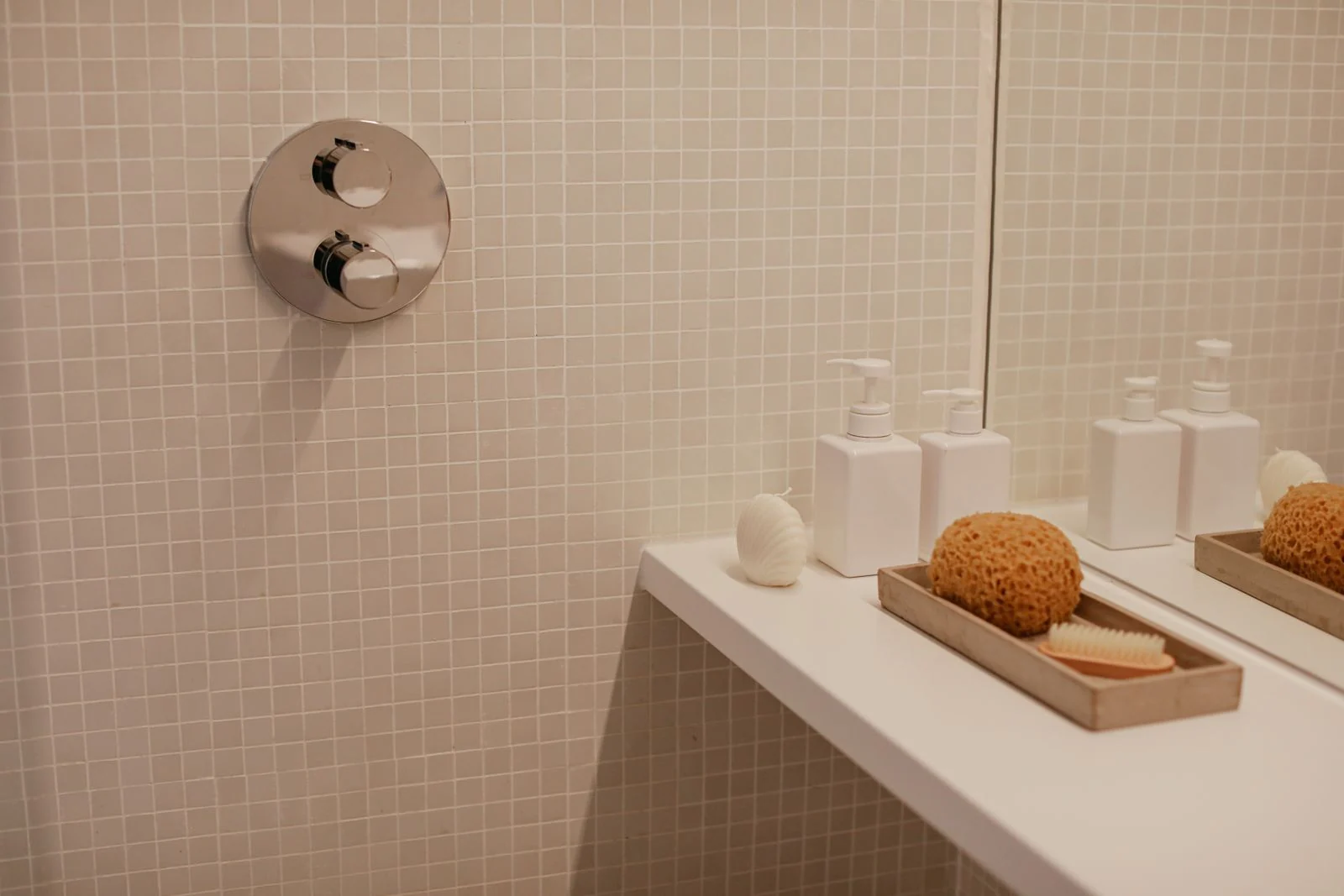 Clean, minimalist bathroom featuring soap dispensers and a loofah on a shelf against a tiled wall
